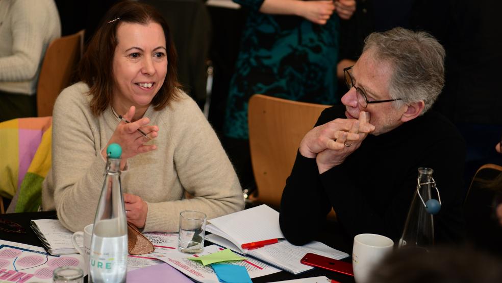 A white woman with short brown hair and a white man wearing glasses discussing civic activity