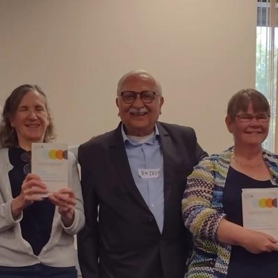 A group of five people standing indoors. Two individuals are holding copies of a book. The person to the far left is holding a microphone.