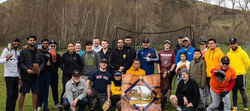 Group shot of the Edinburgh Rays baseball in playing field, standing/crouching around their logo