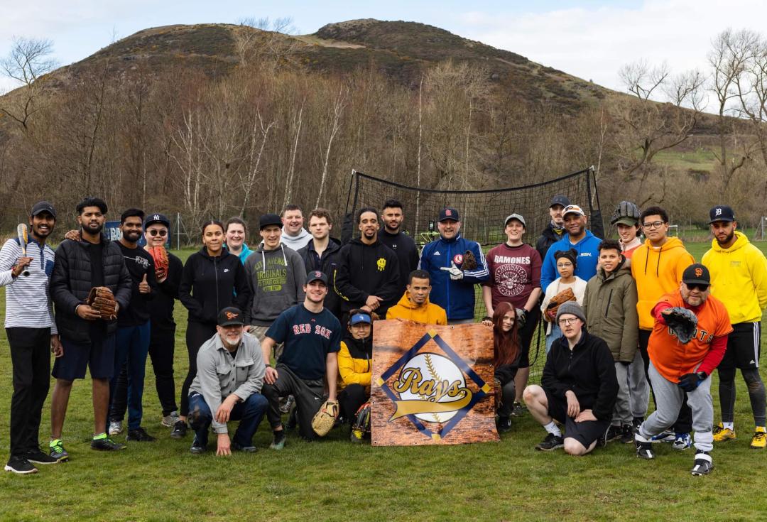 Group shot of the Edinburgh Rays baseball in playing field, standing/crouching around their logo