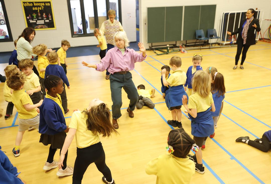 Children moving and dancing around a school hall with their teachers and facilitators