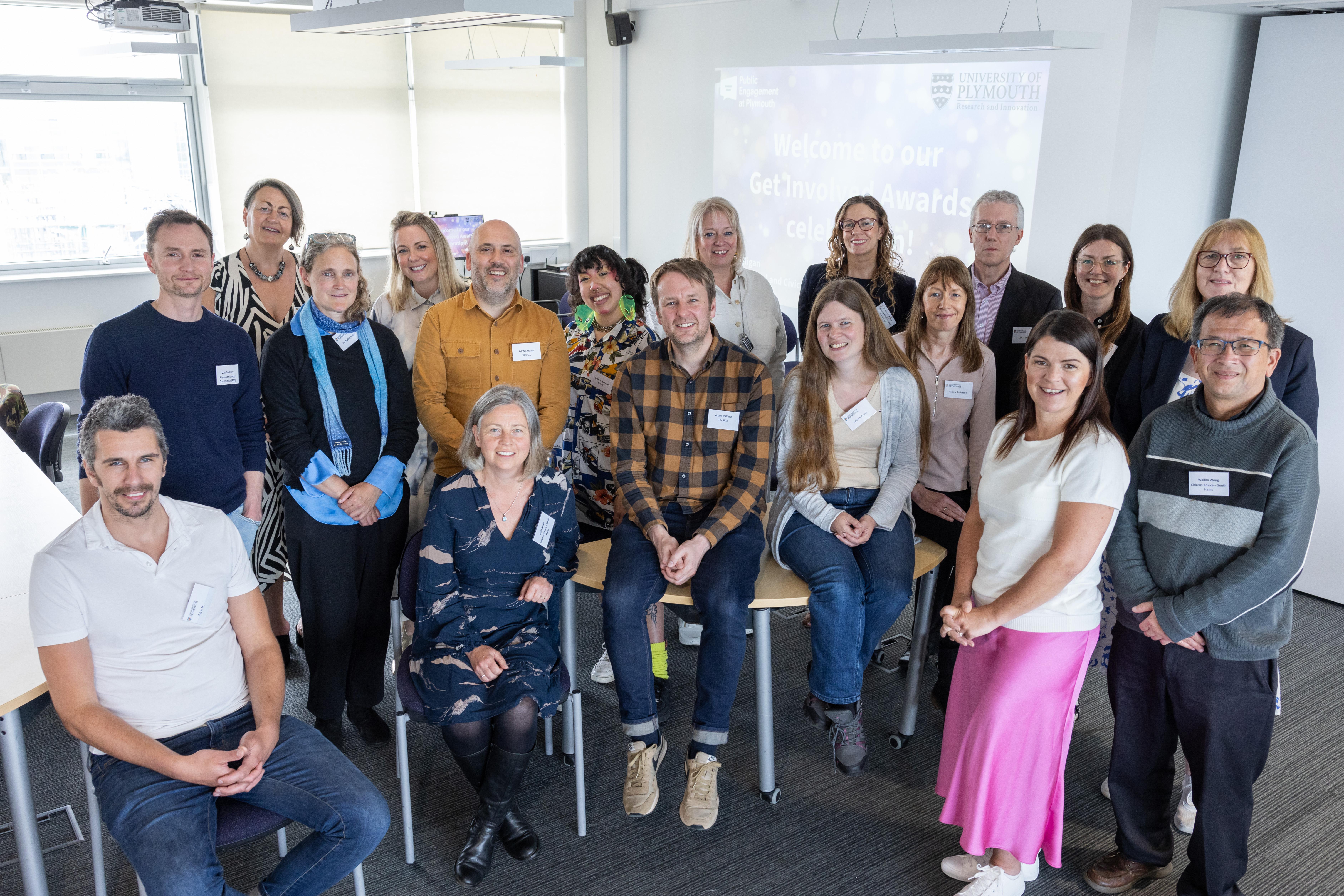 University  of Plymouth staff and members of community groups line up for a photo in a University classroom