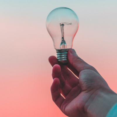 Hand holding on to lightbulb against orange-tinted sky