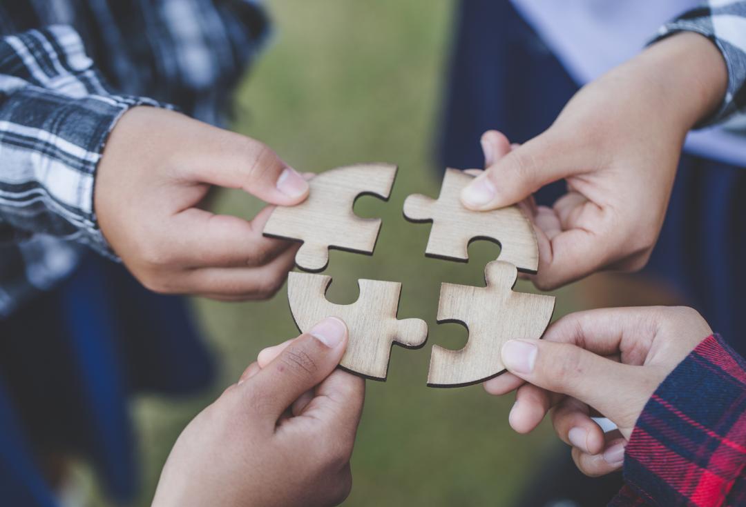 people helping in assembling puzzle, cooperation in decision making, close view of hands connecting pieces.