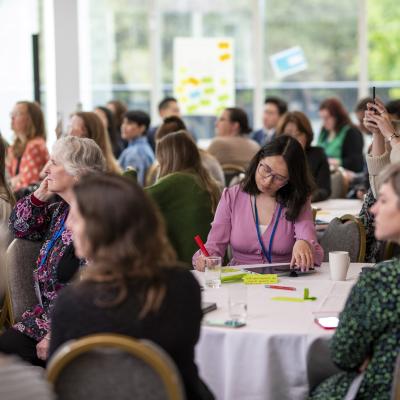 A group of people at Engage conference sitting around tables listening at a panel session