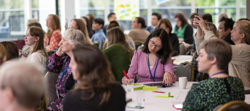 A group of people at Engage conference sitting around tables listening at a panel session