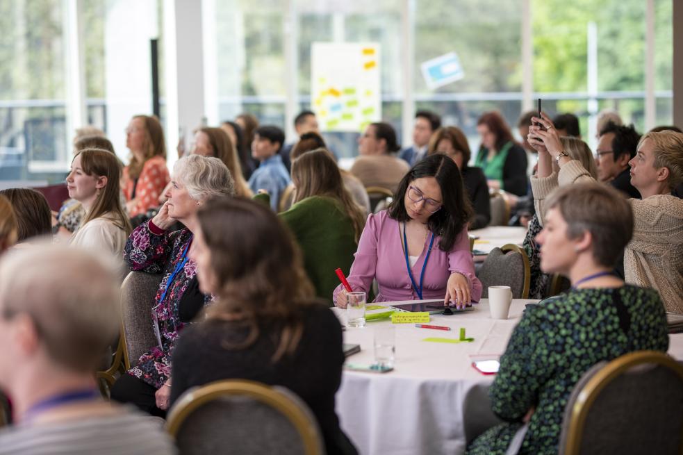 A group of people at Engage conference sitting around tables listening at a panel session