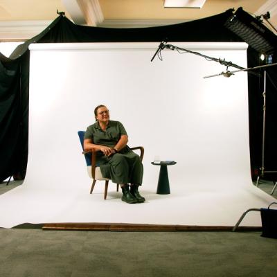 Researcher in a recording studio sat in a chair in front a screen with microphones ready to be filmed