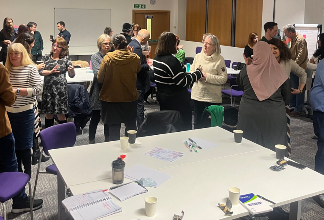 Groups of delegates in discussion, standing in small groups around round tables with notebooks on, in a conference hall